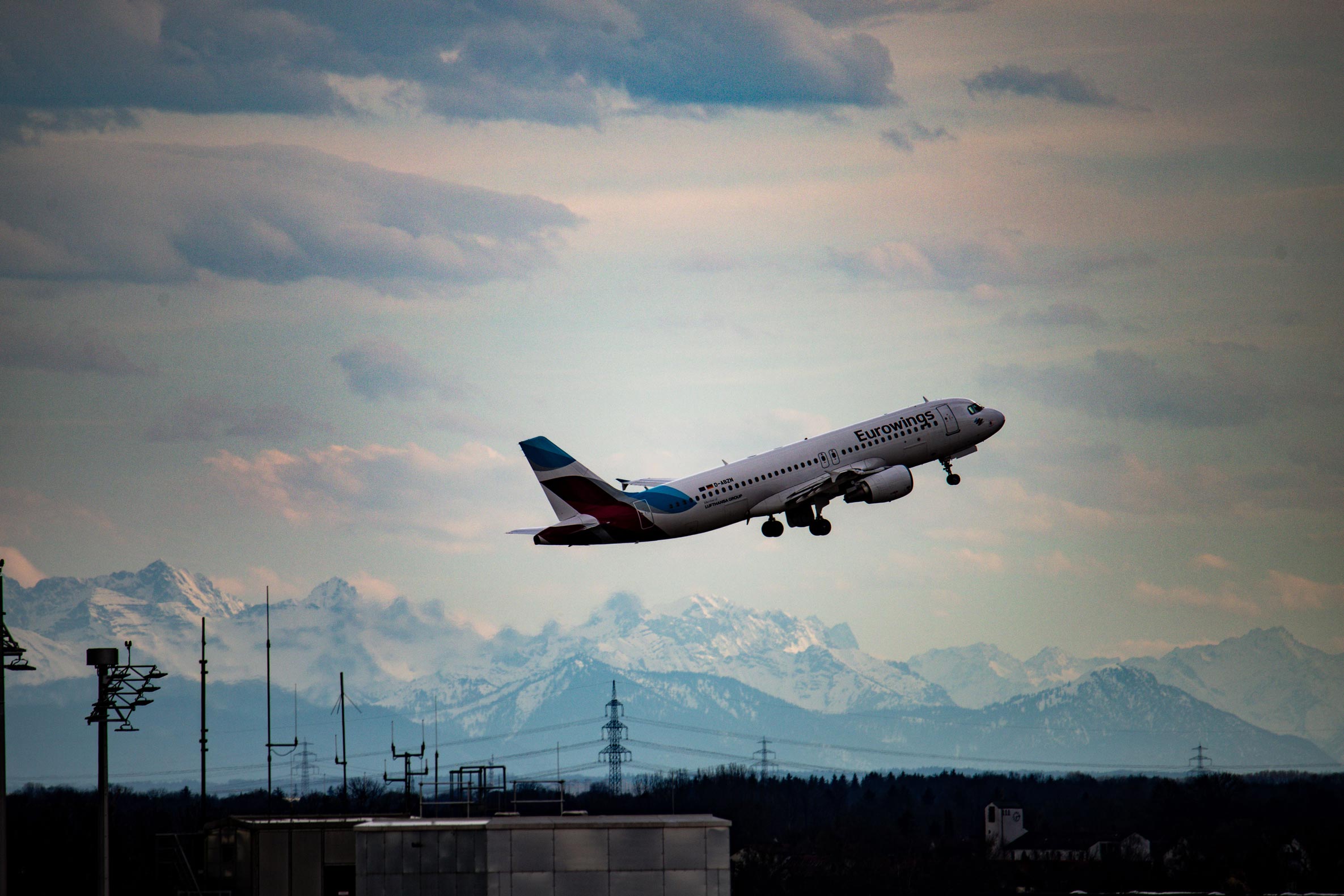 Eurowings Airbus taking off at Munich Airport with snow-capped Alps in the background