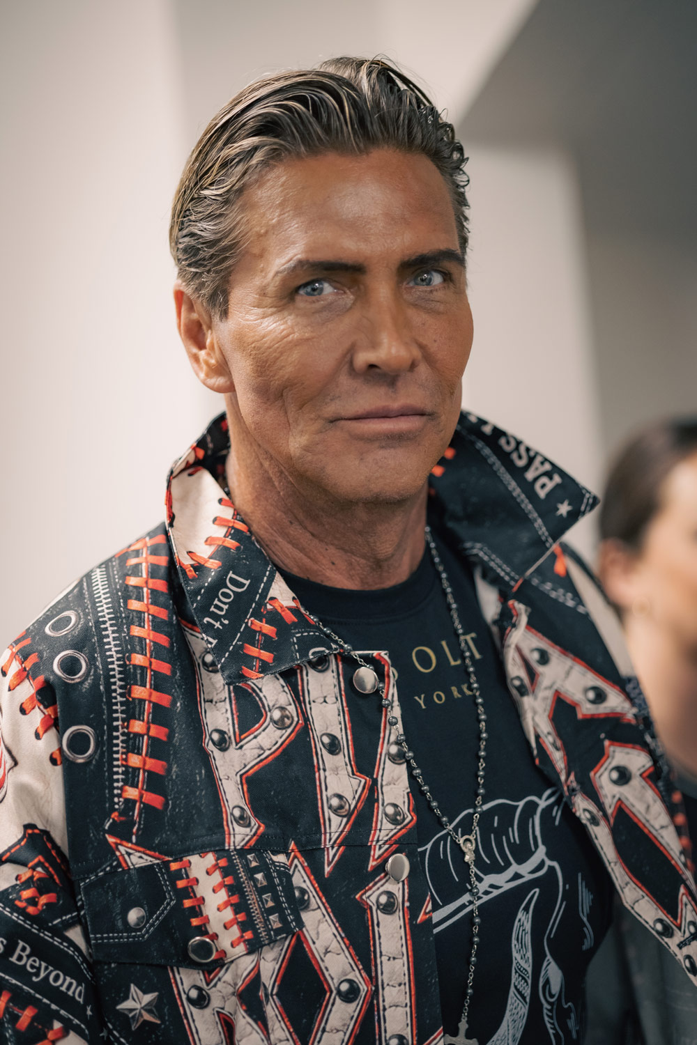 Backstage portrait of an older man with slicked-back hair, wearing a graphic-print jacket from Pia Bolte