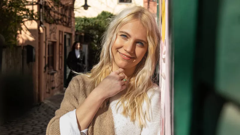 Blonde woman standing next to a wall and smiling into the camera