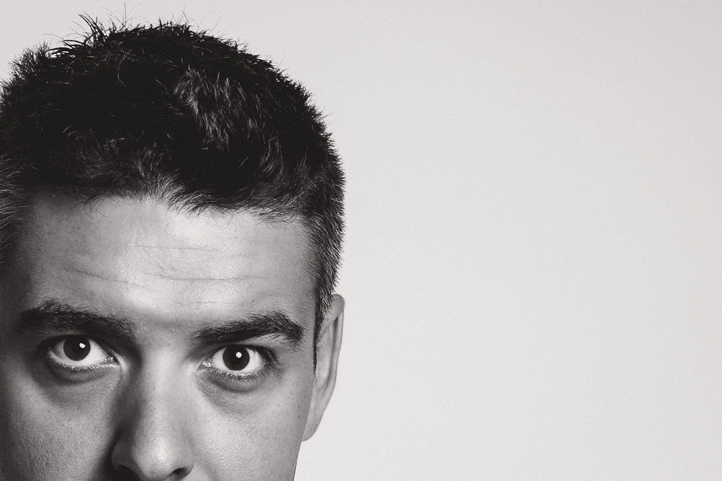 Black and white portrait, upper half of a face with an intense gaze, large area of negative space to the right