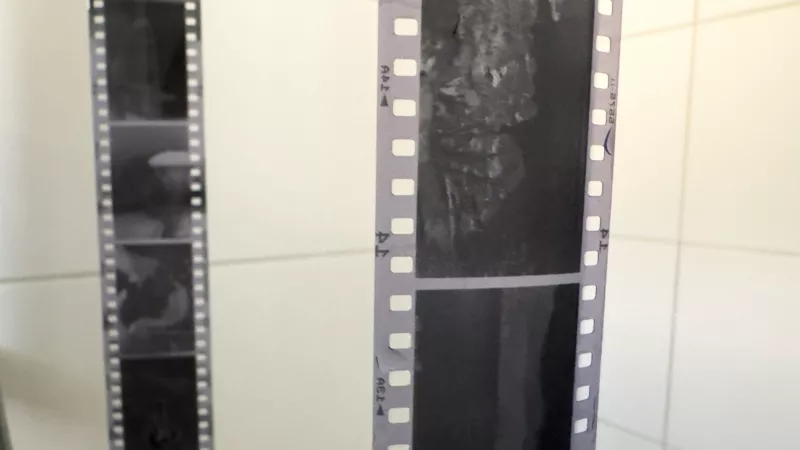 Two developed black and white film strips hanging with clothes pegs on a shower curtain rail