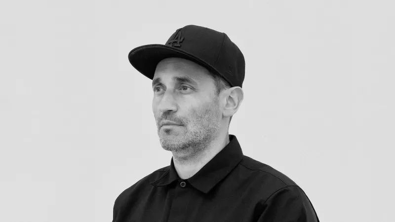 Black-and-white portrait of Jose Navarro, seen from the side, wearing a black cap and a black shirt.