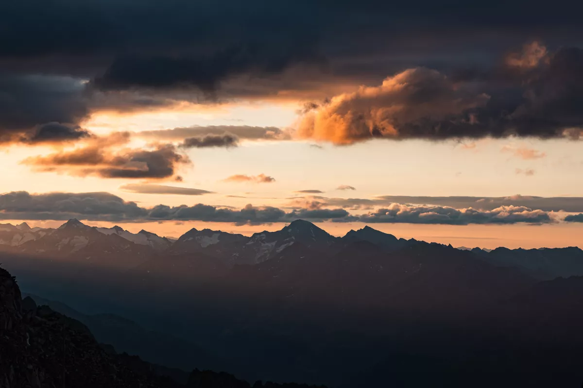 Dramatic sunrise over an alpine mountain range, clouds lit orange at dawn
