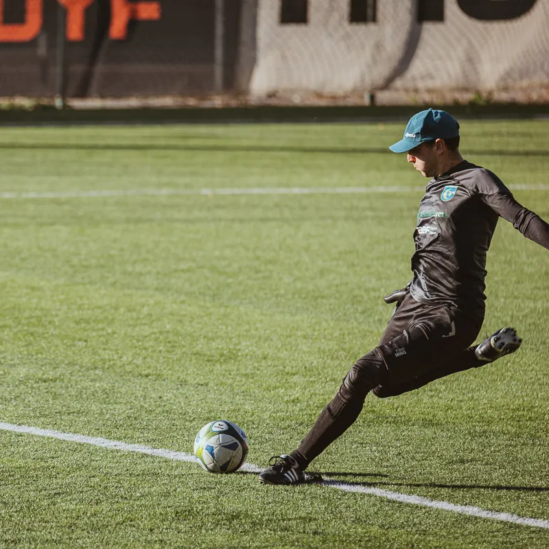 Goalkeeper in black taking a goal kick, the ball still on the line