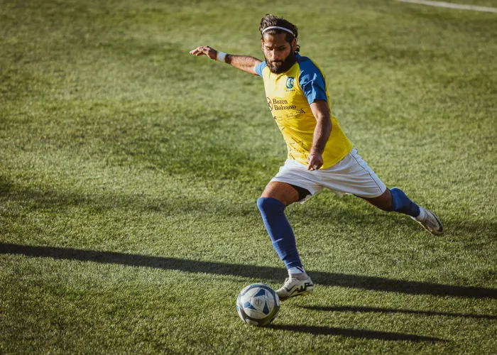 FC Gries player winding up for a shot, arms spread, long shadow on the grass