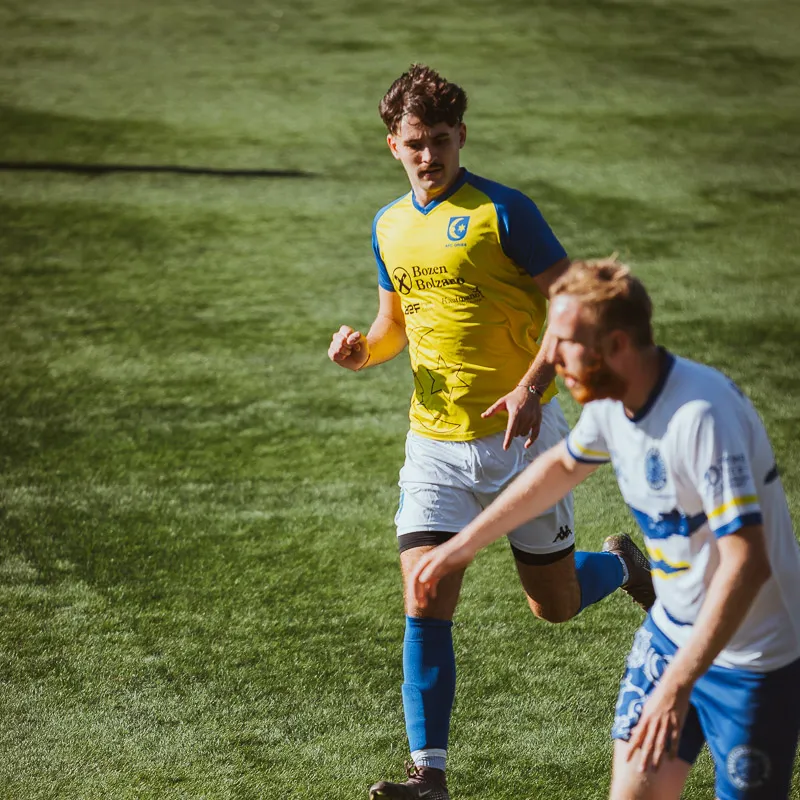 Player in yellow and opponent in white chasing the ball