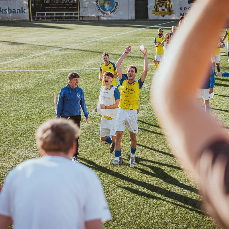 Nach dem Abpfiff jubeln Mannschaft und Betreuer zu den Fans, vorn ein erhobener Arm