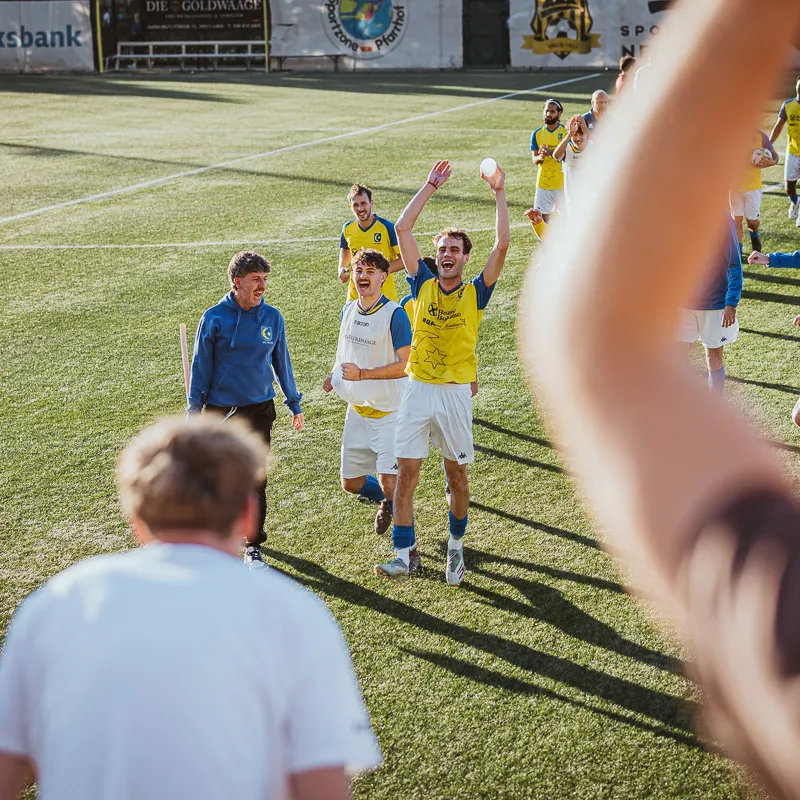 After the final whistle, team and staff celebrate toward the fans, a raised arm in the foreground