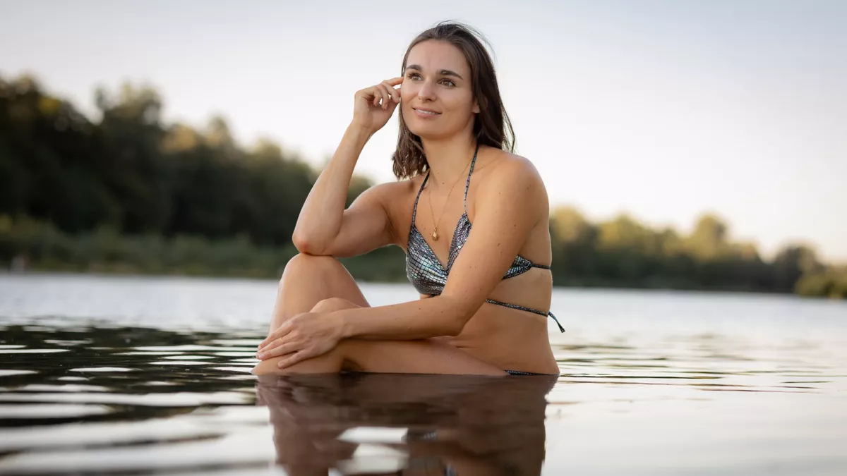 A woman in a sparkly bikini sits smiling in the water