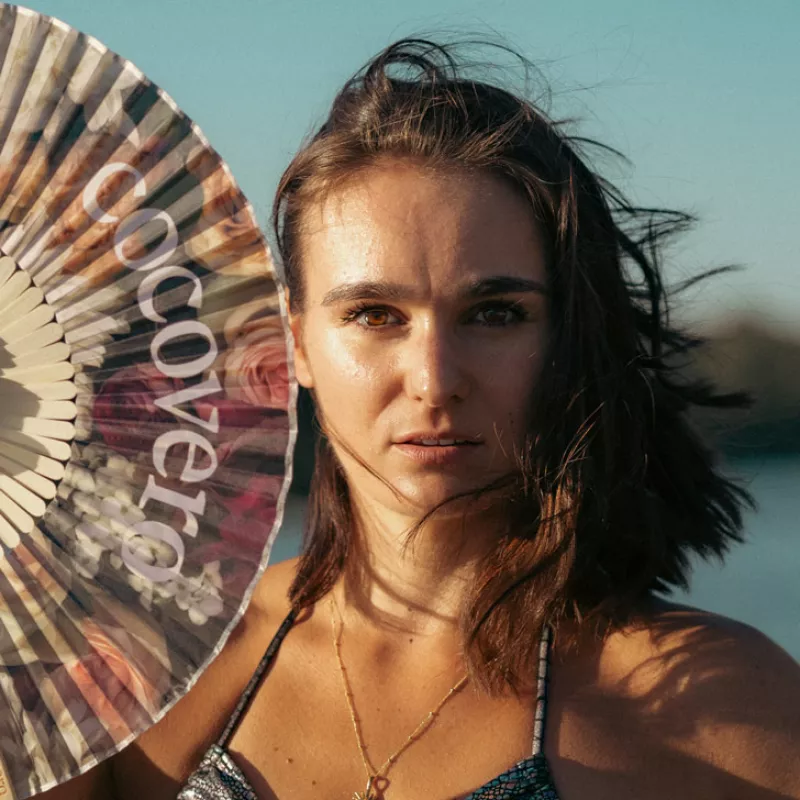 A close-up of a woman in a sparkly bikini holding a fan that reads "cocovero".