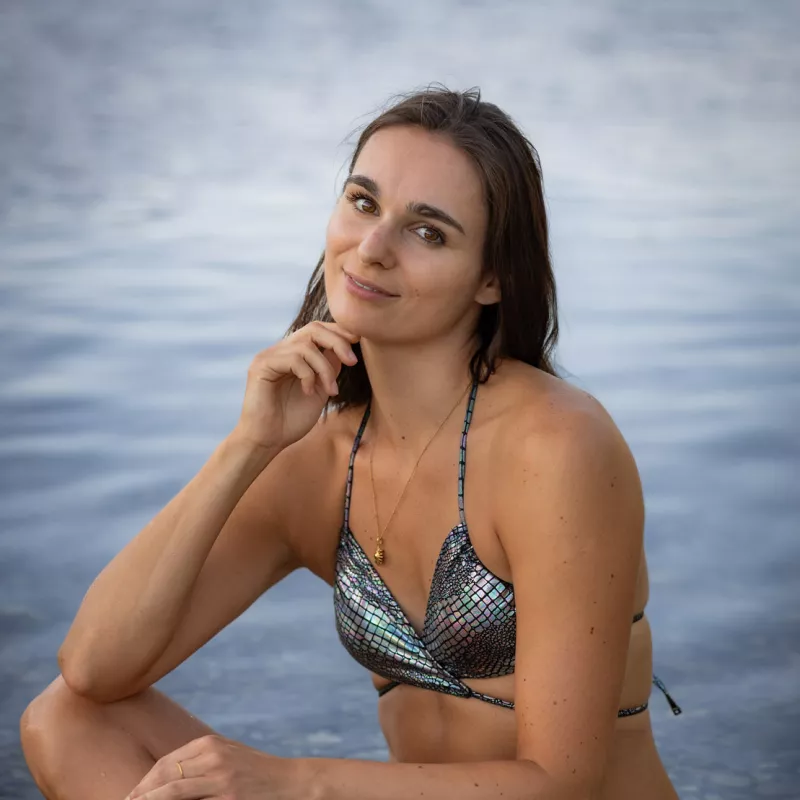 A woman in a sparkly bikini sits in the water, looking upwards.