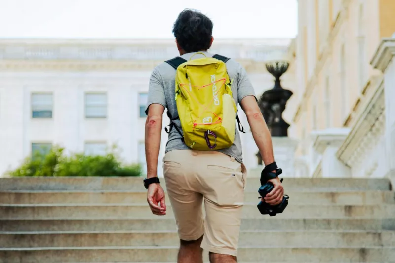 A man with a backpack and a camera in his hand is walking up a staircase in Boston