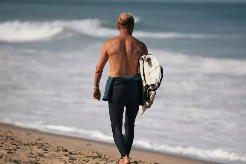 A surfer is walking along the beach at Cape Cod